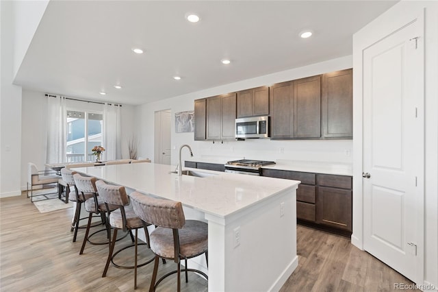 kitchen with light wood finished floors, an island with sink, a sink, stainless steel appliances, and a kitchen bar