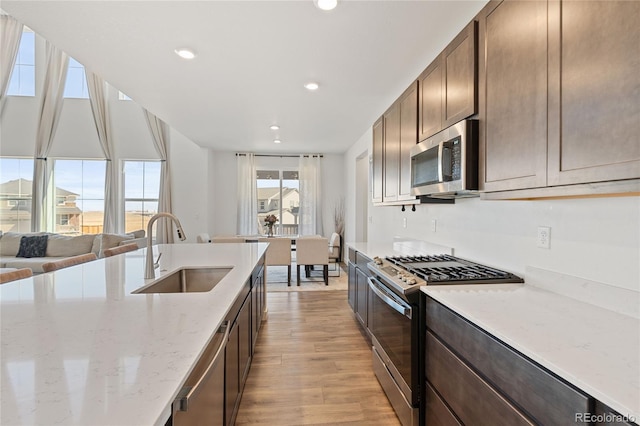 kitchen with a sink, light wood-type flooring, dark brown cabinetry, and appliances with stainless steel finishes