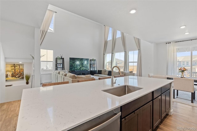 kitchen featuring light wood finished floors, dark brown cabinetry, light stone counters, and a sink