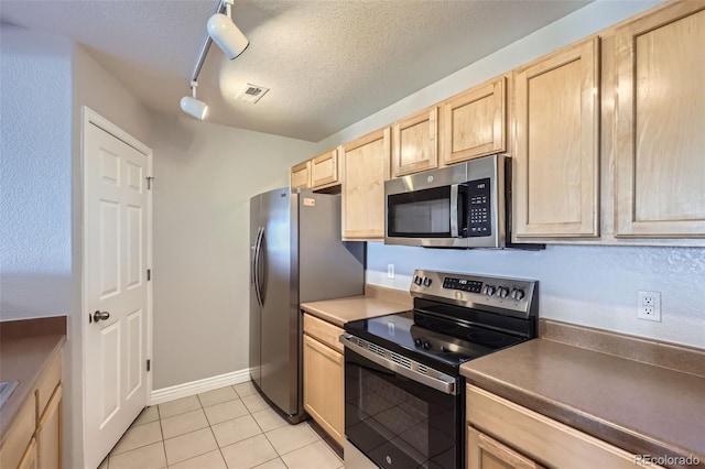 kitchen featuring light brown cabinetry, a textured ceiling, light tile patterned floors, track lighting, and appliances with stainless steel finishes