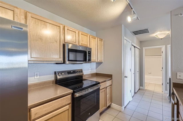 kitchen featuring light tile patterned floors, stainless steel appliances, track lighting, a textured ceiling, and light brown cabinetry