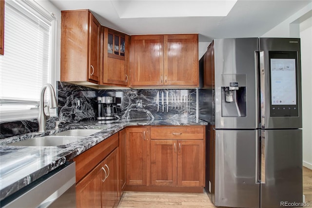 kitchen with dark stone countertops, a sink, stainless steel appliances, brown cabinets, and backsplash