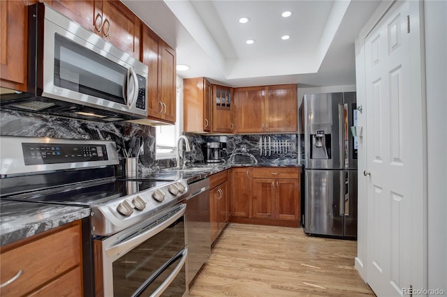 kitchen with backsplash, brown cabinetry, light wood finished floors, and stainless steel appliances