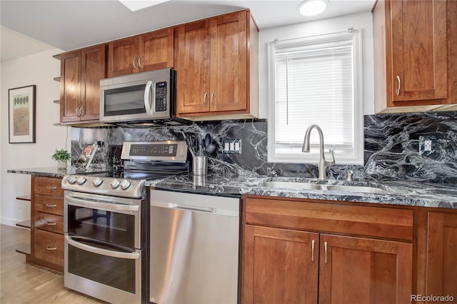 kitchen with dark stone countertops, brown cabinetry, a sink, appliances with stainless steel finishes, and tasteful backsplash