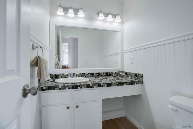 half bath featuring vanity, toilet, wood finished floors, and a wainscoted wall