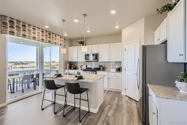 kitchen featuring white cabinets, decorative light fixtures, stainless steel appliances, and a center island with sink