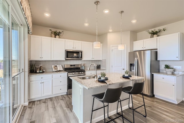 kitchen with a kitchen island with sink, white cabinets, sink, light stone countertops, and stainless steel appliances