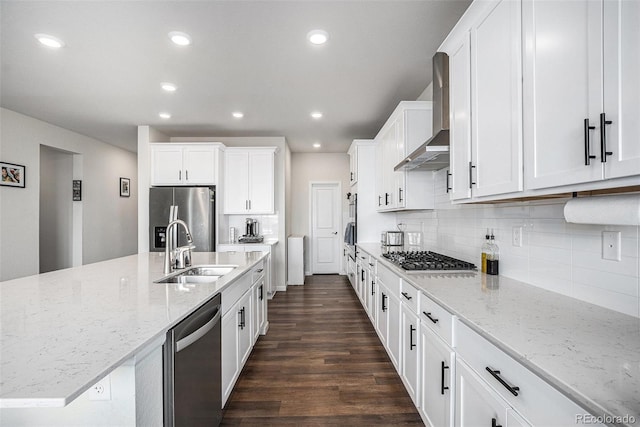 kitchen featuring wall chimney range hood, dark wood finished floors, a sink, stainless steel appliances, and white cabinetry