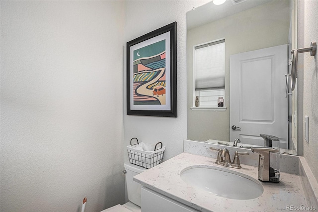 half bath featuring toilet, a textured wall, and vanity