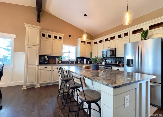 kitchen with a wainscoted wall, lofted ceiling with beams, appliances with stainless steel finishes, glass insert cabinets, and a kitchen island