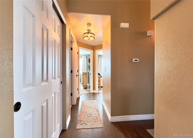 hall featuring baseboards, wood finished floors, and a textured wall