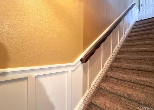 stairway with wainscoting, a decorative wall, and a textured wall