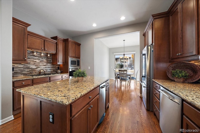 kitchen featuring dark wood-type flooring, a kitchen island, pendant lighting, stainless steel appliances, and light stone countertops