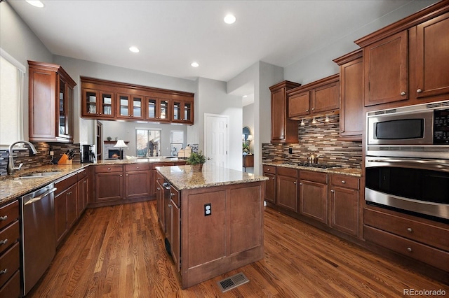 kitchen featuring sink, a center island, light stone counters, stainless steel appliances, and dark wood-type flooring