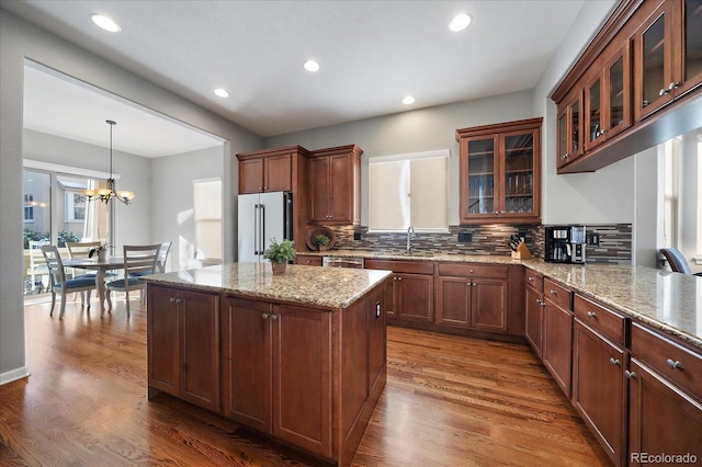 kitchen with pendant lighting, wood-type flooring, sink, stainless steel appliances, and light stone countertops