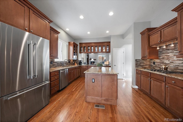 kitchen featuring light hardwood / wood-style flooring, a kitchen island, stainless steel appliances, light stone countertops, and backsplash