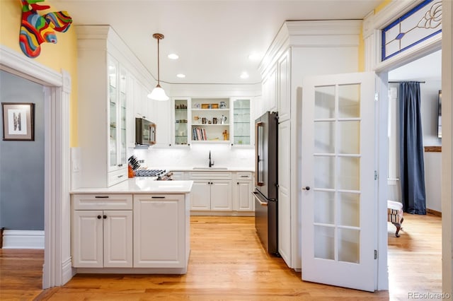 kitchen featuring appliances with stainless steel finishes, pendant lighting, sink, white cabinets, and light hardwood / wood-style floors