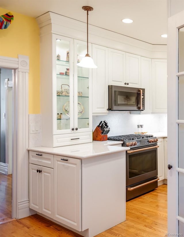 kitchen with stainless steel appliances, white cabinetry, pendant lighting, and light hardwood / wood-style floors