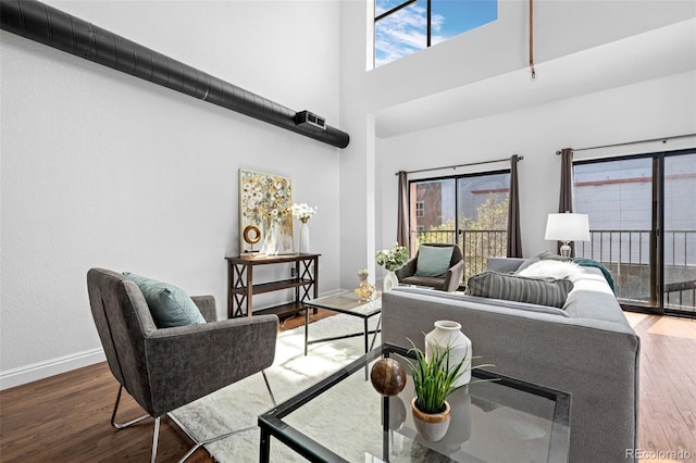 living area with baseboards, a high ceiling, wood finished floors, and a healthy amount of sunlight