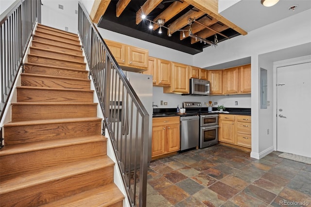 kitchen featuring stone tile flooring, dark countertops, baseboards, electric panel, and appliances with stainless steel finishes