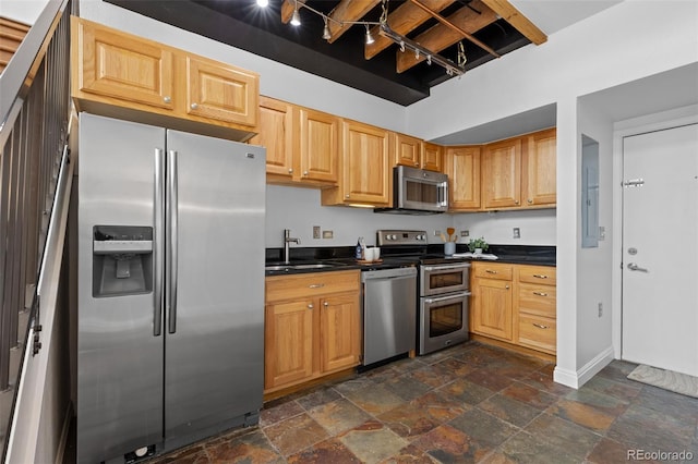 kitchen featuring dark countertops, appliances with stainless steel finishes, a sink, and stone tile flooring