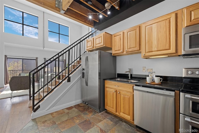 kitchen featuring dark countertops, baseboards, stone finish floor, a sink, and stainless steel appliances