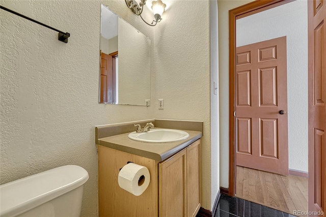 bathroom with a textured wall, wood finished floors, vanity, and toilet