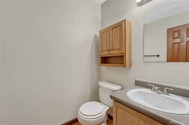 bathroom featuring toilet, a textured wall, and vanity