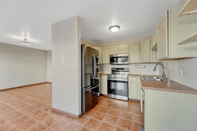 kitchen with light tile patterned floors, stainless steel appliances, a sink, green cabinets, and light countertops