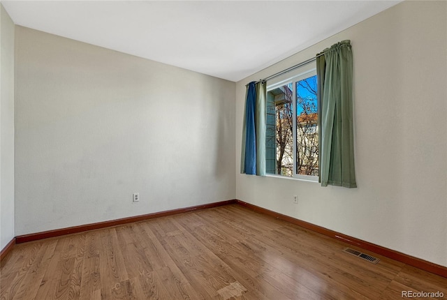 empty room with baseboards, visible vents, and light wood finished floors