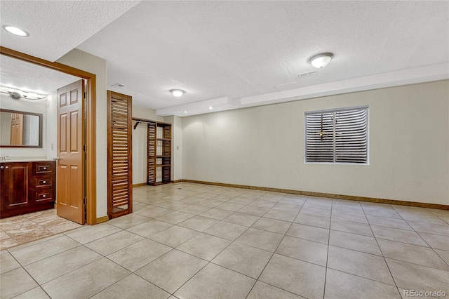 basement with a textured wall, a textured ceiling, baseboards, and light tile patterned floors