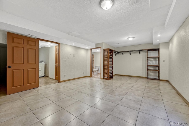 finished below grade area featuring a textured ceiling, a textured wall, light tile patterned floors, baseboards, and washer / clothes dryer