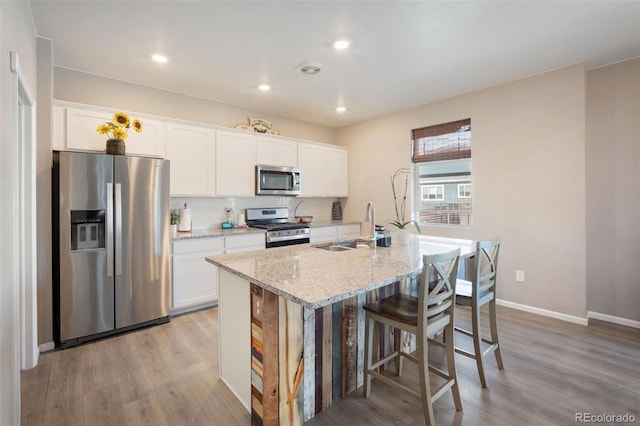 kitchen featuring tasteful backsplash, an island with sink, sink, white cabinets, and stainless steel appliances