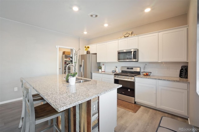 kitchen featuring sink, stainless steel appliances, white cabinets, and a center island with sink