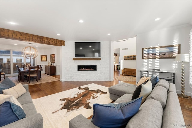 living room with hardwood / wood-style flooring, a notable chandelier, and a stone fireplace