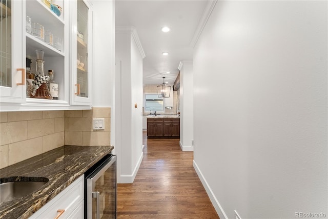 hallway featuring dark wood-type flooring, beverage cooler, crown molding, and a chandelier