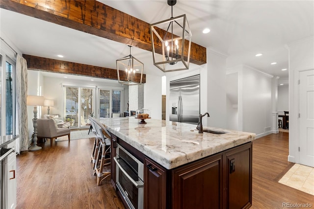 kitchen with appliances with stainless steel finishes, an island with sink, sink, hanging light fixtures, and a chandelier