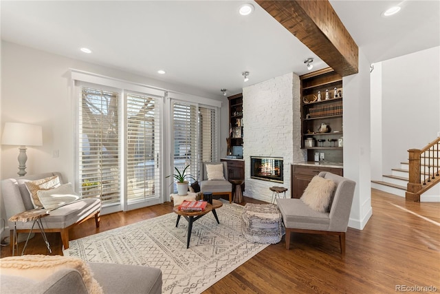 living room featuring built in shelves, wood-type flooring, a fireplace, and a healthy amount of sunlight