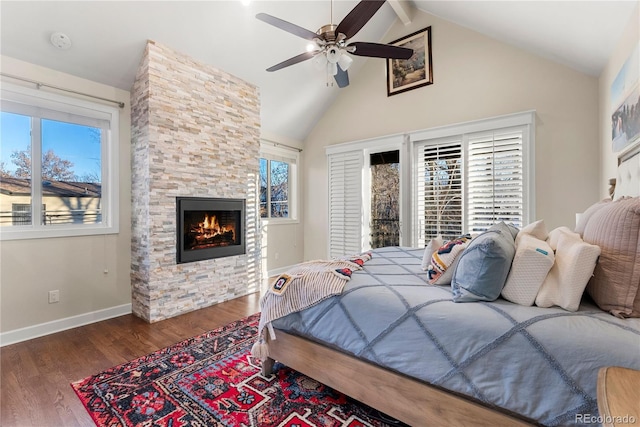 bedroom with ceiling fan, dark hardwood / wood-style floors, a stone fireplace, and vaulted ceiling with beams