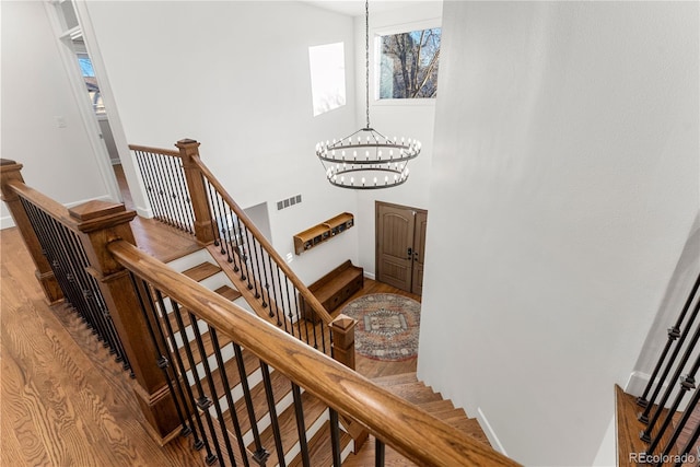 stairway with a high ceiling, hardwood / wood-style floors, and a chandelier