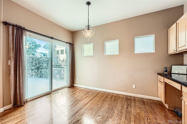 unfurnished dining area with an inviting chandelier and light wood-type flooring