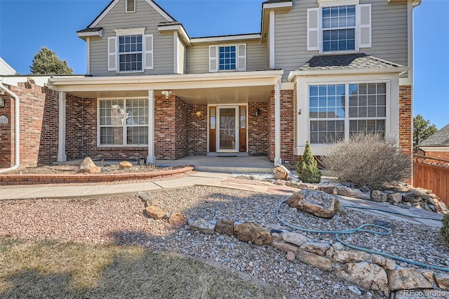 traditional-style home featuring a porch, brick siding, and fence