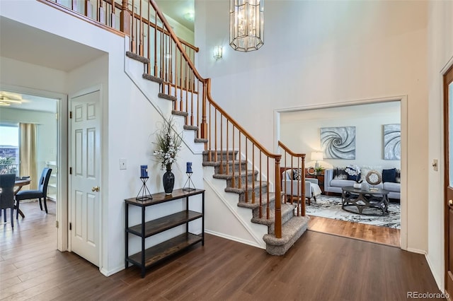 entrance foyer with baseboards, stairway, dark wood-style flooring, a high ceiling, and a chandelier