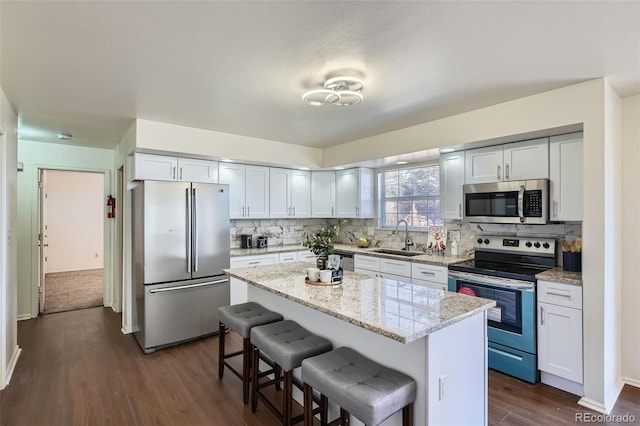 kitchen with decorative backsplash, appliances with stainless steel finishes, a kitchen breakfast bar, dark wood-type flooring, and a sink