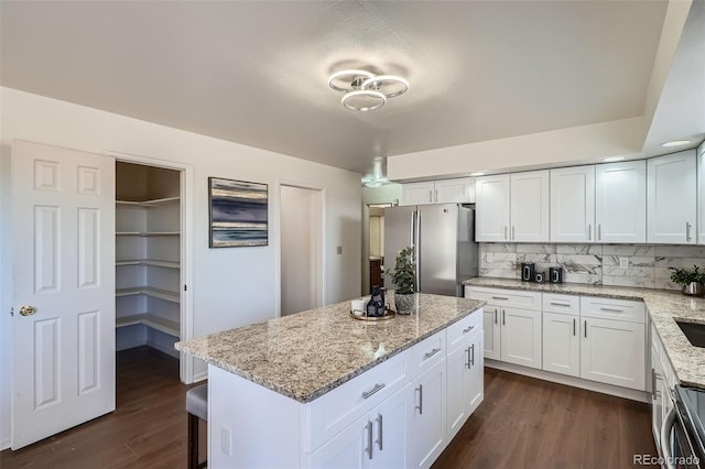 kitchen with dark wood-type flooring, white cabinetry, freestanding refrigerator, light stone countertops, and tasteful backsplash