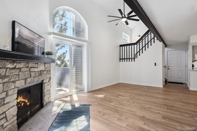 unfurnished living room with a ceiling fan, a stone fireplace, wood finished floors, baseboards, and high vaulted ceiling