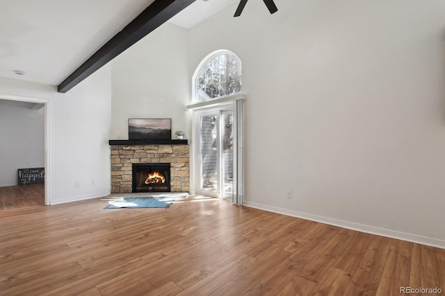 unfurnished living room with beamed ceiling, a ceiling fan, a stone fireplace, high vaulted ceiling, and wood finished floors