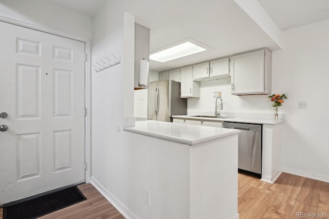 kitchen with stainless steel appliances, a sink, baseboards, and light wood-type flooring