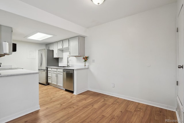 kitchen featuring appliances with stainless steel finishes, a sink, baseboards, and light wood-style flooring
