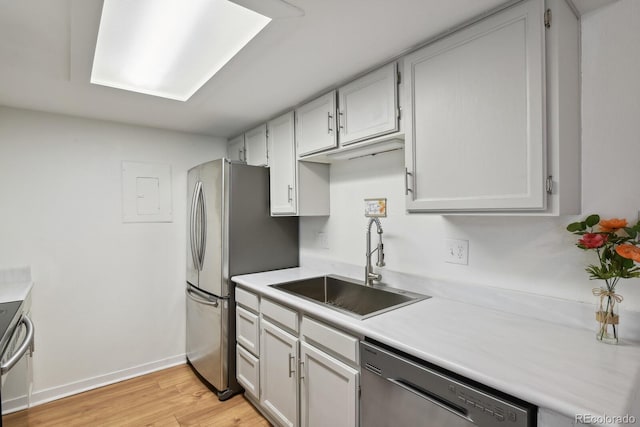 kitchen featuring appliances with stainless steel finishes, a sink, light countertops, light wood finished floors, and baseboards